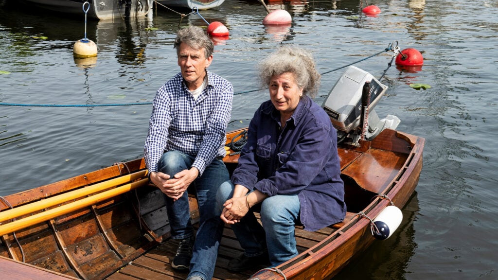 En man och en kvinna sitter i en mahognyeka som ligger i vattnet.