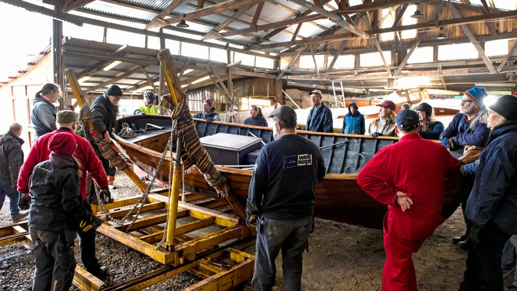 Cirka 20 personer står runt en träsnipa inne i en äldre träbyggnad.