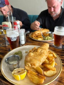 Några män äter fish and chips. På bordet står också glas med öl i.