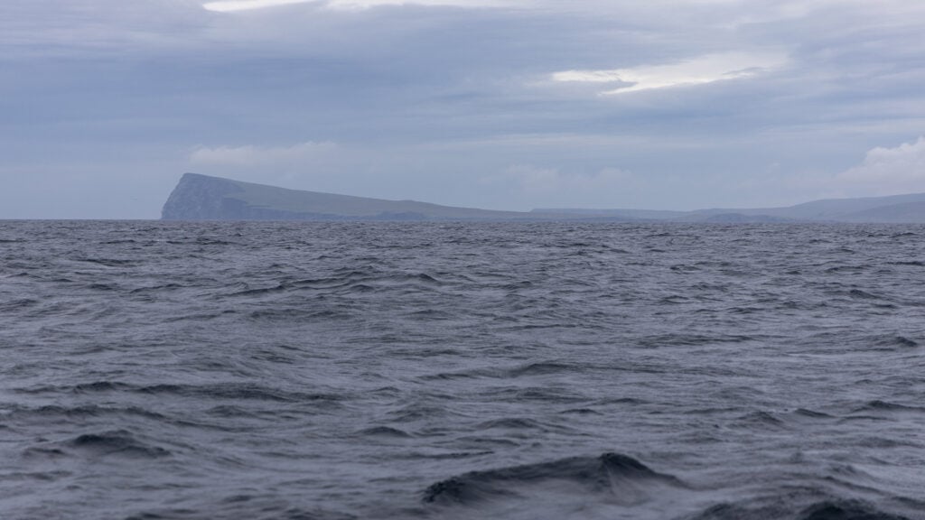 Disigt och gråmulet över havet. I fjärran ser man en ö med en klippa med brant sluttning ner mot havet i den vänstra delen.