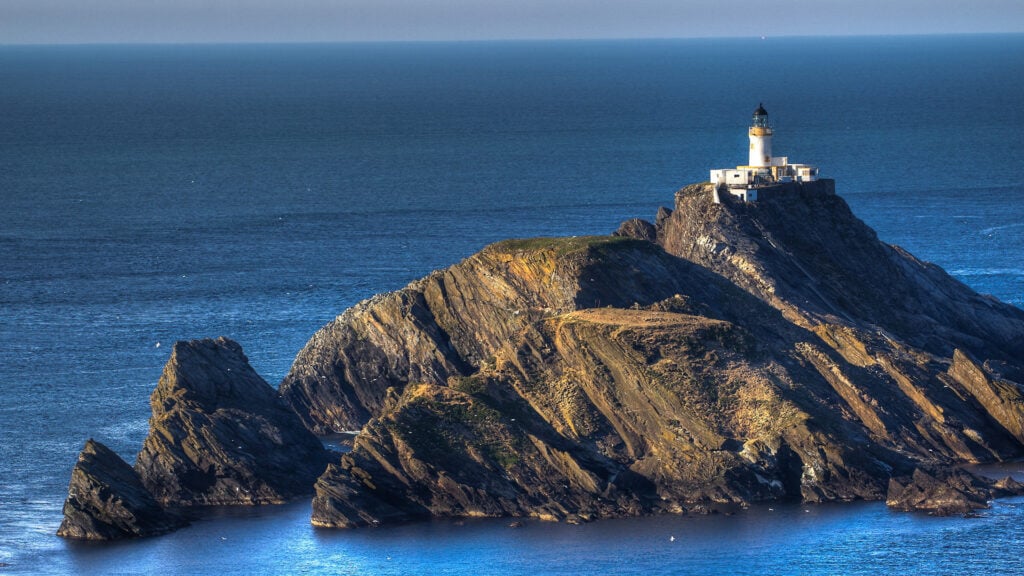 En fyr längst upp på en klippig ö mitt ute i havet.