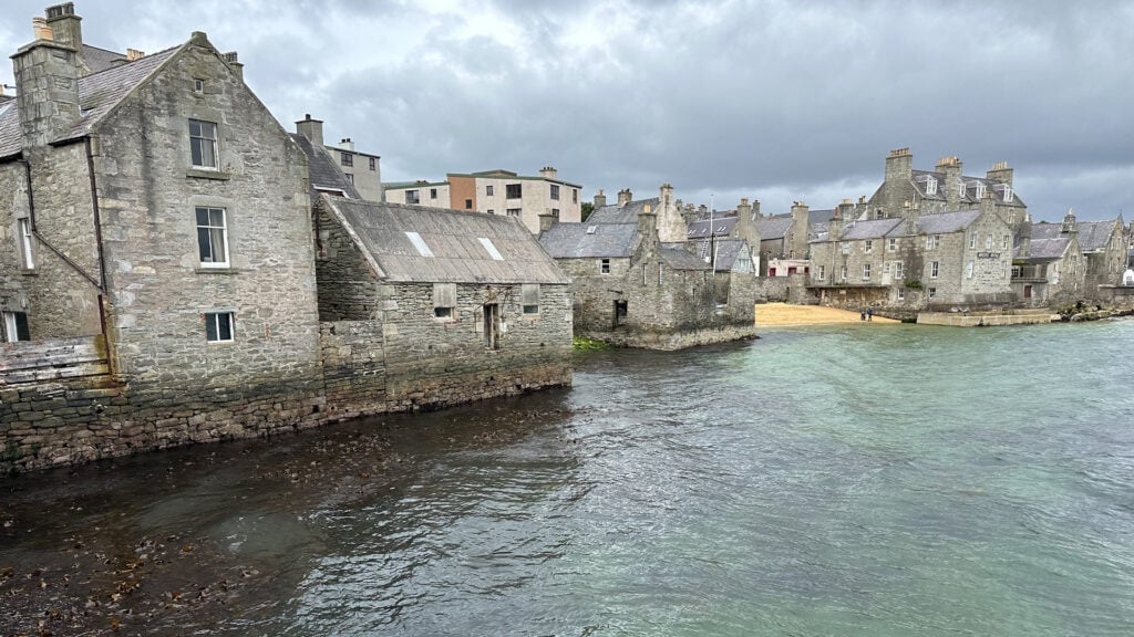 Äldre, grå hus precis vid havet.