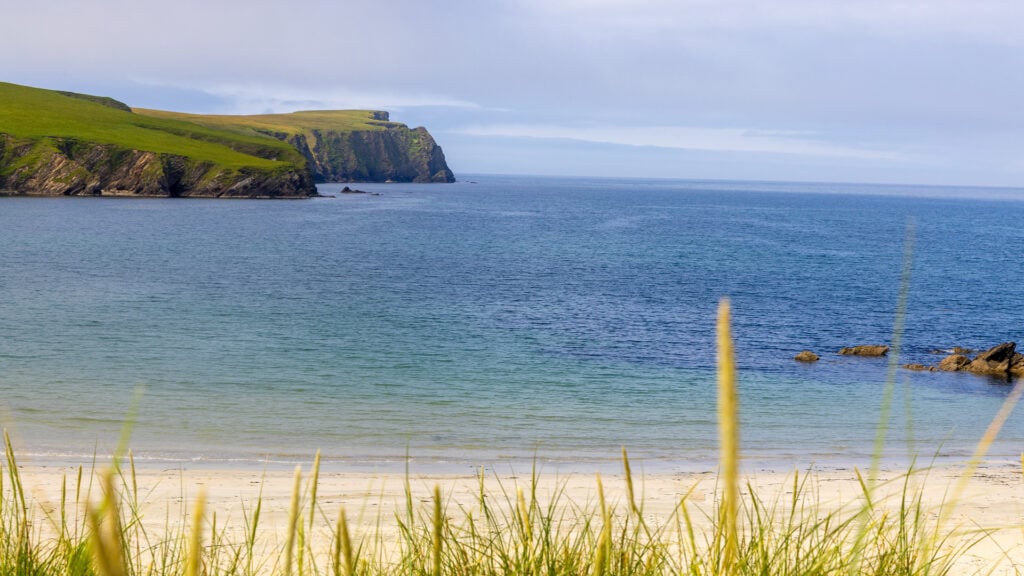 Vacker utsikt från en sandstrand. Till vänster gräsbeklädda klippor som sticker ut i havet.