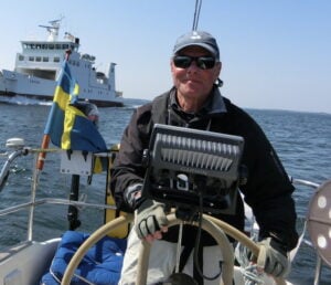 En man i flytväst vid rodret på en segelbåt ute till havs.