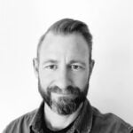 En medelålders man med mörkt skägg och kort hår i sidbena.