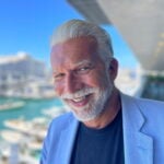 En solbränd man i övre medelåldern med vitt hår och välansat vitt skägg.