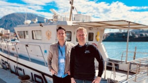 Två män framför en större motorbåt vid en norsk fjord.